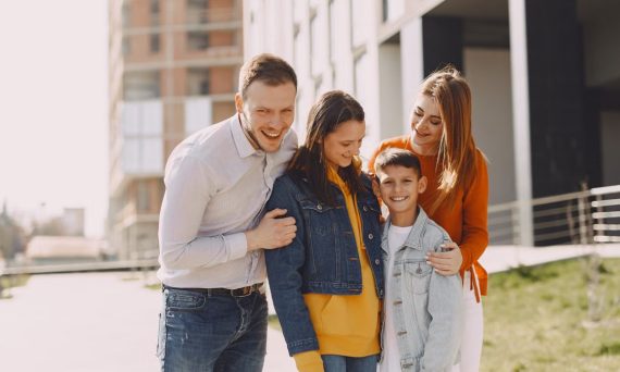 Delighted family in trendy casual wear holding each other and standing near modern building on city street while walking together during weekend